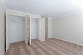 Bedroom with light walls & neutral carpet & a wide closet with two sets of double doors with hanging rods & upper shelves.