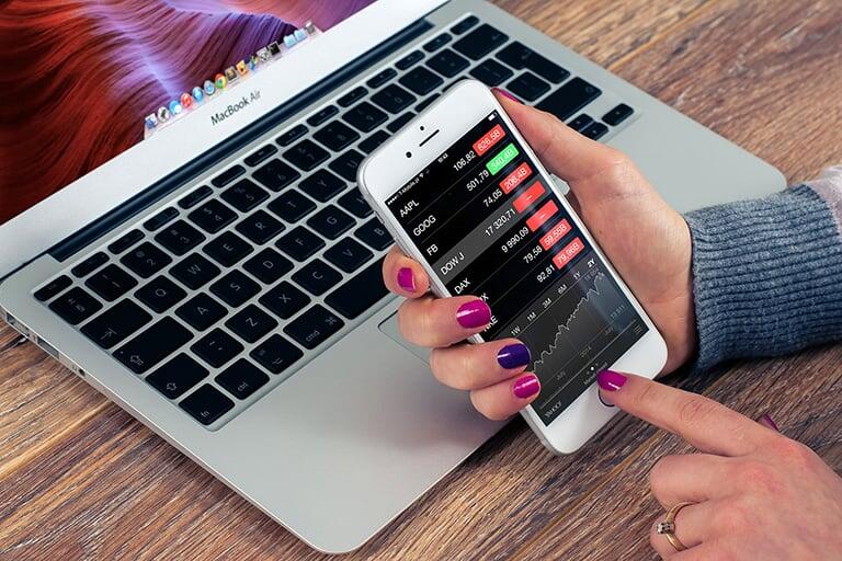 A lady holding open her iphone looking over stocks.