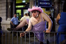 man in paarse jurk en netkousen staat met een voet op een hek dat hij vasthoudt