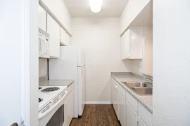 Fully-equipped galley-style kitchen with wood-style flooring, white cabinets, and white appliances