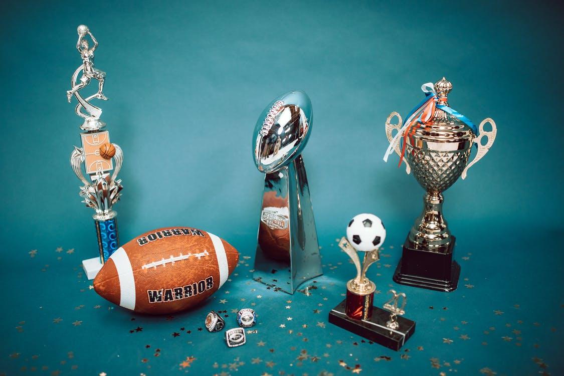 Sports trophies and a football placed on a teal background