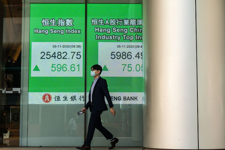 A pedestrian walks past an electronic screen displaying the Hang Seng Index, left, and the Hang Seng China Industry Top Index in Hong Kong. Picture: BLOOMBERG/CHAN LONG HEI