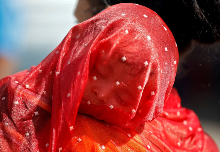 A migrant worker covers her child with a sari to protect him from heat as she waits in a queue for transport to reach to a railway station to board a train to her home state of northern Uttar Pradesh, after a limited reopening of India's giant rail network following a nearly seven-week lockdown to slow the spreading of the Covid-19 coronavirus, in Ahmedabad, India, on May 16, 2020.