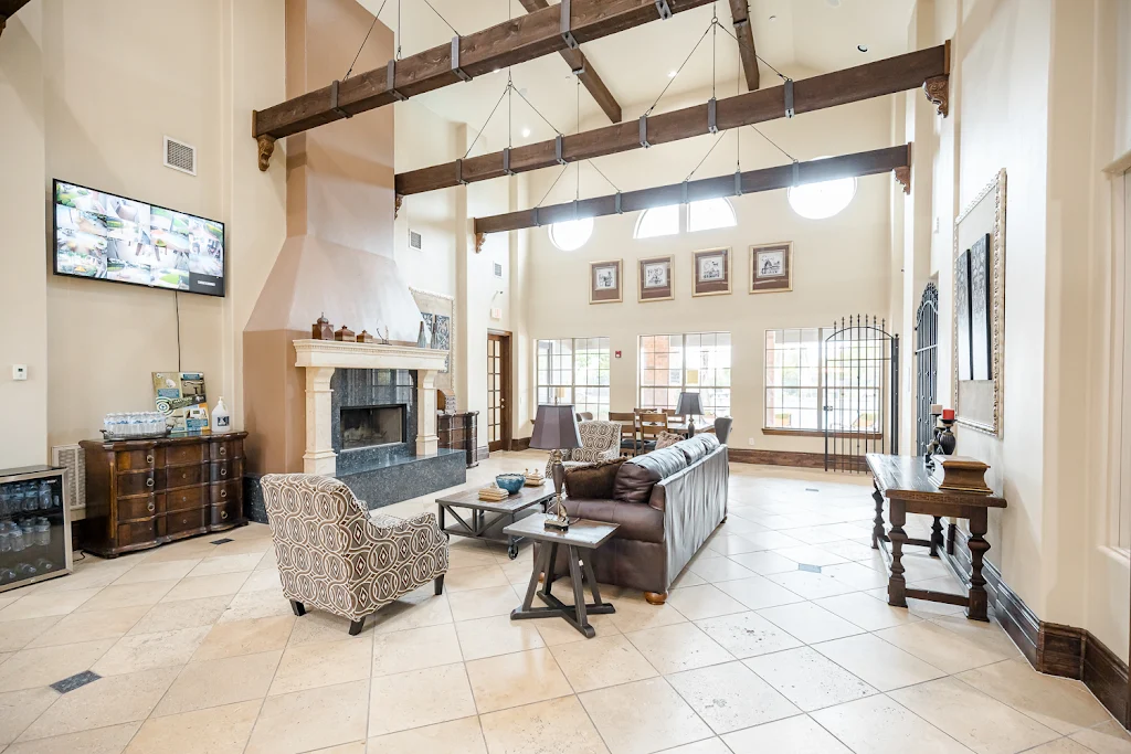 Clubhouse lounge area with high ceilings with wood beams, tile flooring, couch, chairs, fireplace, and mounted TV