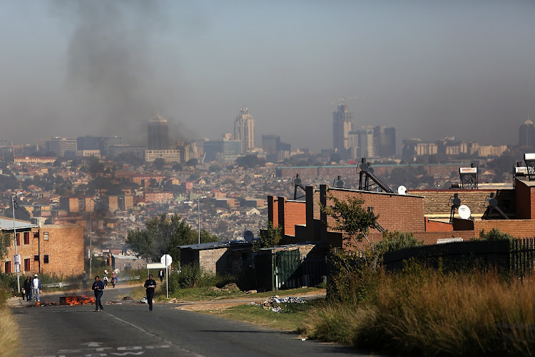 APRIL 25, 2018. People walk on the road in Alexandra, Johannesburg. A barricaded road forms the backdrop.