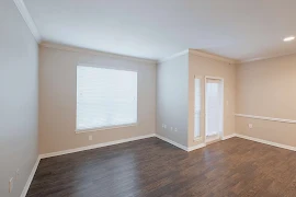 Living room with windows with blinds, patio door, wood plank flooring, light beige walls, and white trim