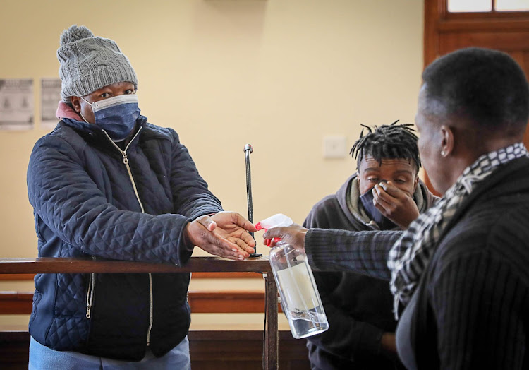 Modiehi Mofokeng, pictured with co-accused Thabo Moji, a Lesotho citizen who was charged for contravening Immigration Laws, gets sanitised at the Fouriesburg magistrate's court in the Free State.