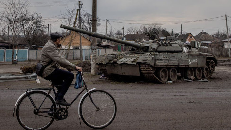 A man rides past a destroyed Russian tank in Trostyanets, north-east Ukraine