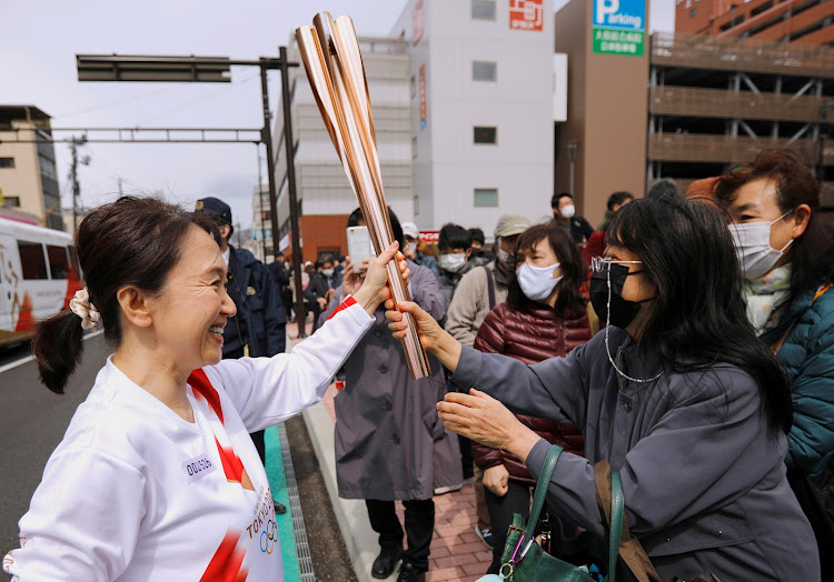 Spectators try to touch the torch carried by torchbearer Junko Ito, after her run during the Tokyo 2020 Olympic torch relay on the second day of the relay in Fukushima, Japan March 26, 2021.