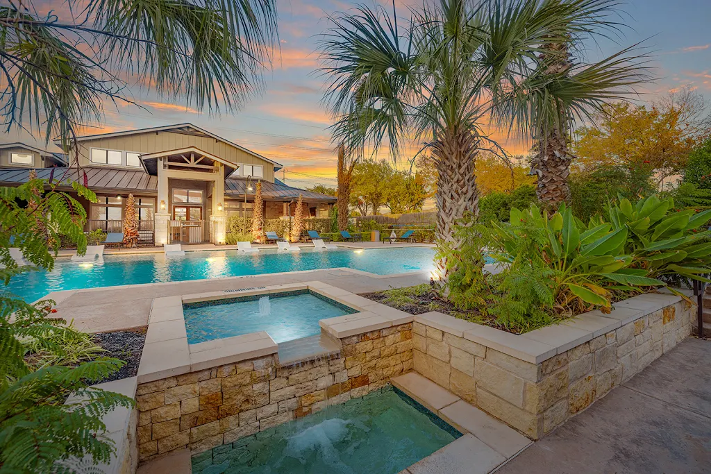 Bridge at Southpark Meadows community pool with clubhouse in background surrounded by lush tropical landscaping at dusk