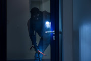 A thief with a flashlight trying to break a door.