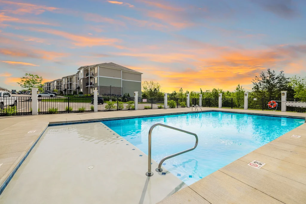 Apartment complex with outdoor pool at sunset, colorful sky, comfortable lounging chairs, and well-kept garden surroundings.