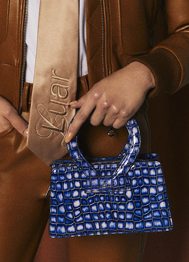 A close up of Charles Gross's hand holding a blue Luar bag.