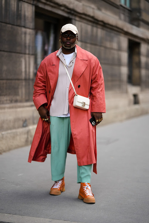 A guest wears a white denim cap from Balenciaga, a white t-shirt, a gray embossed striped pattern shirt, a red long trench coat outside the Wooyoun show, during Paris Fashion Week - Menswear Spring/Summer.