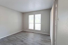 Living room with dark grey wood floors, two large windows, sliding patio doors with blinds