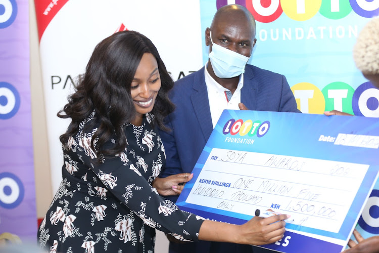 Lotto Foundation CEO Joan Mwaura signs a cheque of Ksh 1.5 million towards the Soya Awards as 2008 Olympic 800m champion Wilfred Bungei looks on