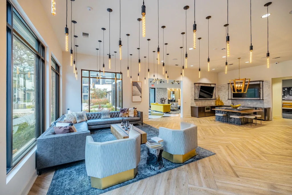 Clubhouse lounge with seating areas, mounted TVs, pendant lighting, light wood flooring, and modern decor