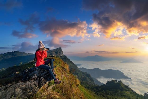 Traveller sitting on the rock and holding camera take photo at doi pha mon mountains in chiang rai, thailand Free Photo