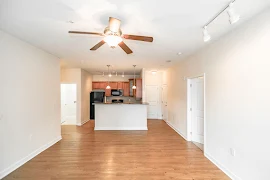 Living and dining area has a wood floor, light-colored walls, ceiling fan, track light, and a view of the open kitchen ahead