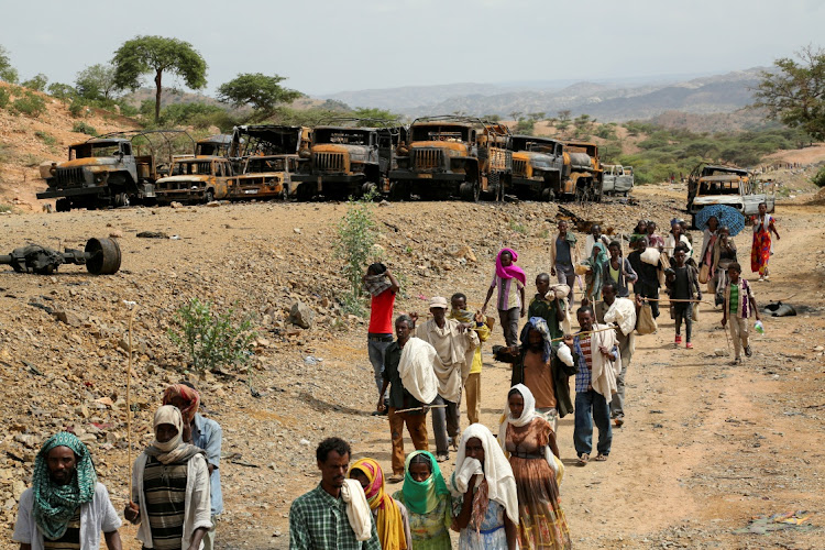 Villagers return from a market to Yechila town in south central Tigray walking past scores of burned vehicles, in Tigray, Ethiopia, in this July 10 2021 file photo. REUTERS/GIULIA PARAVICINI