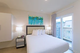 Model bedroom with plush white comforter, neutral colored walls, and access the balcony