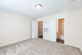 Bedroom with light carpet and white walls, attached bathroom, walk in closet, and central light fixture