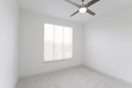 Bedroom with light walls, grey trim, plush carpet, large window for natural lighting, and a ceiling fan