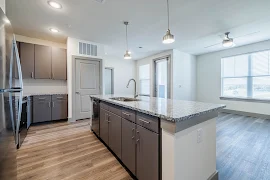 Modern kitchen in an apartment with stainless steel appliances, dark cabinets, and pendant lights.