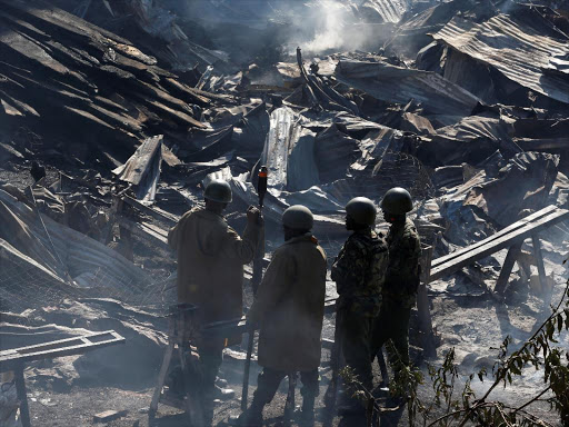 Riot police stand at the smouldering scene of fire that gutted down the timber dealership of the Gikomba market and nearby homes in central Nairobi./REUTERS.