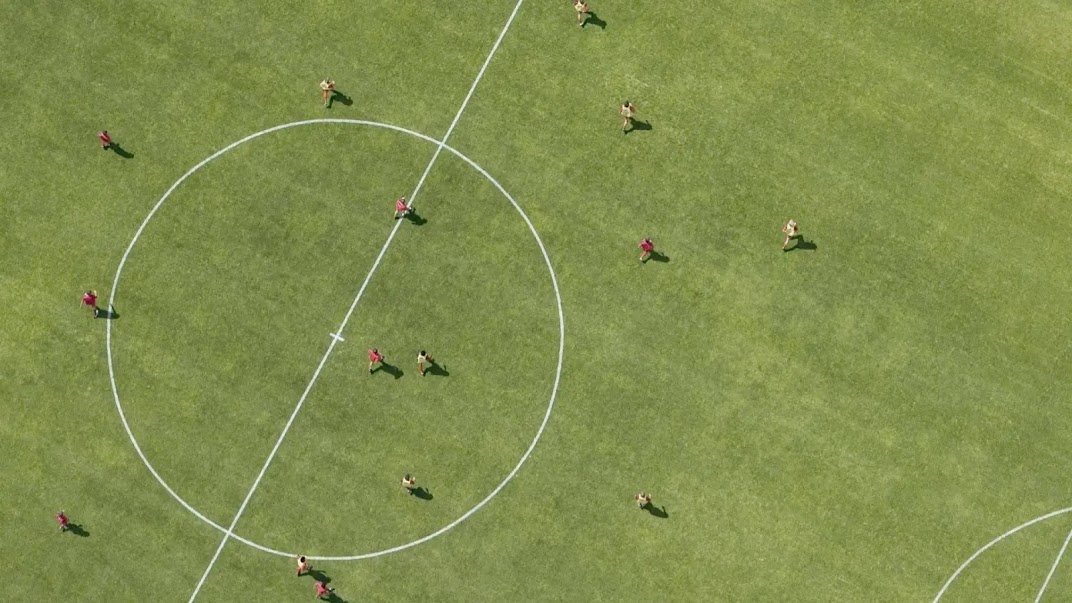 A photo showing a section of a soccer pitch, shot from above. Fourteen players are visible, running or walking.