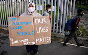 Cape Flats resident Farieda Abrahams from Hanover Park, Western Cape stands outside the gate of her son's school protesting agains the reopening of schools as Covid-19 infections are on a rapid rise on July 7 2020. 