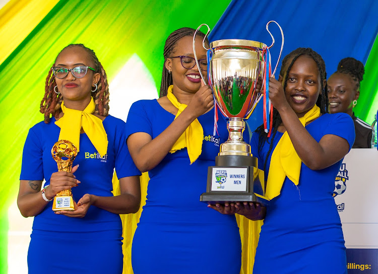 Models showcase the winners' trophies for the Meru Football Challenge