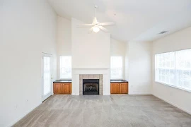 Large, open living room features fireplace between two windows with built in cabinets beneath, next to a door to the patio