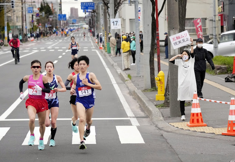 In this file picture, a spectator raises a placard reading "It is impossible to hold the Olympics, face up to reality" along the race route during the half-marathon as part of Hokkaido-Sapporo Marathon Festival 2021, a testing event for the Tokyo 2020 Olympics marathon race, amid the coronavirus disease (COVID-19) pandemic, in Sapporo, Hokkaido Prefecture, Japan on May 5, 2021