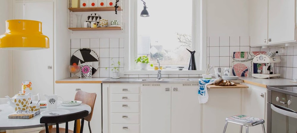 Fotografía de una pequeña cocina blanca retro con una mesa de comedor y una ventana.