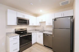 Kitchen with stone countertops, stainless steel appliances, white cabinets, and wood-inspired flooring