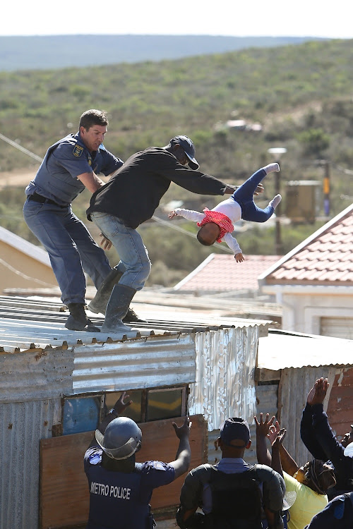 A Nelson Mandela Bay metro police officer grabs the father as he throws his child off the roof of a shack at the Joe Slovo informal settlement in Port Elizabeth on 12 April 2018.