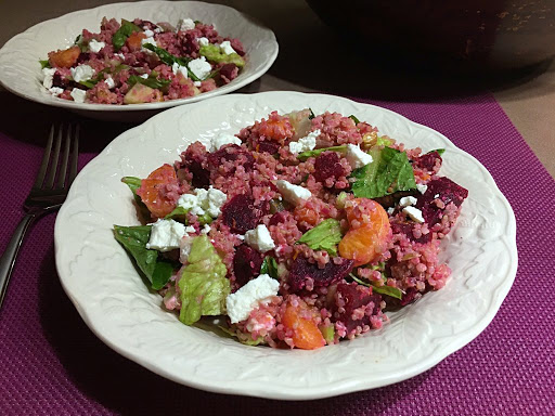 A salad with quinoa, beets, mandarin oranges and cheese served in a white bowl.