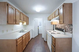 Kitchen with light wood cabinets, white countertops, white appliances, dark wood floors, connected to laundry room