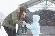 Kathrine Williams puts gloves on her daughter Katie Williams, aged 5 while they play in the snow, 10 July 2023, at Jackson Dam in Alberton, South of Johannesburg.   