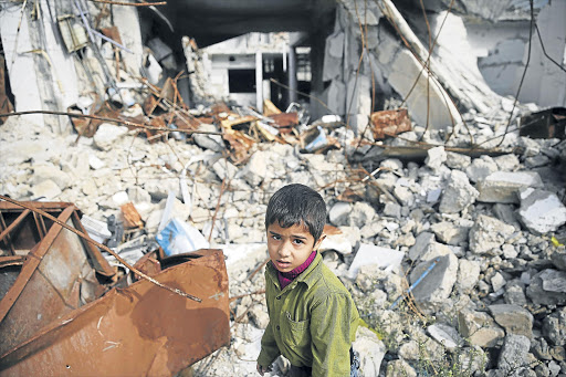 INNOCENT VICTIM: A boy walks amid damaged buildings in the town of Douma, eastern Ghouta in Damascus, Syria, this week Picture: REUTERS