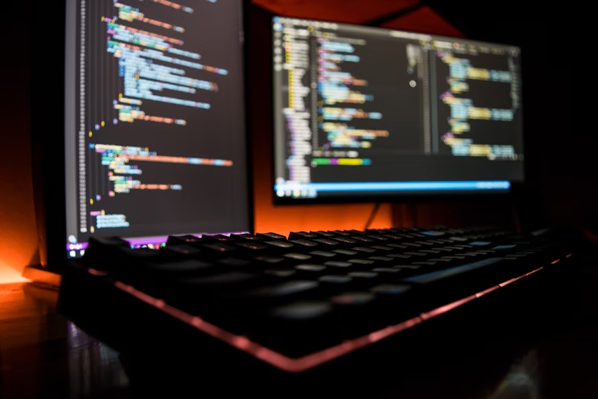 A back computer keyboard and two different screens with lines of codes