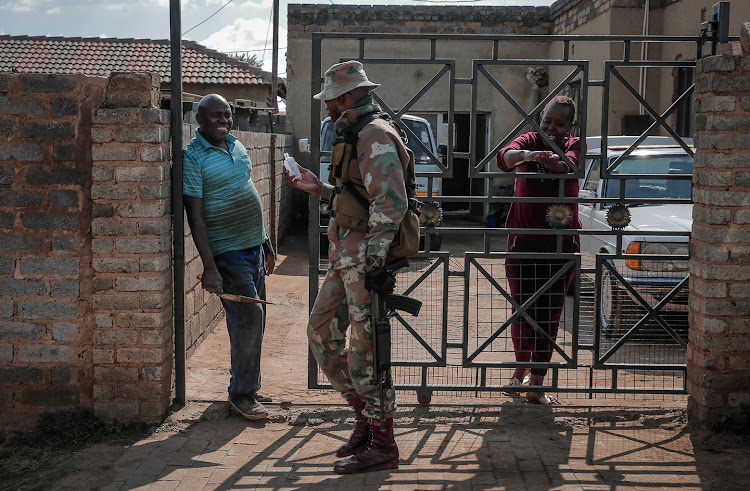 A member of the SANDF offers hand sanitiser to residents while patrolling the streets of Soweto to enforce lockdown regulations. During the patrol they checked permits and made several arrests and confiscated goods.