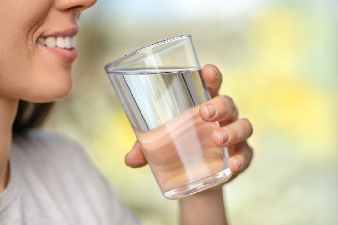 Mengatasi Batuk muda duduk di sofa sambil minum teh herbal dari cangkir besar untuk meredakan batuknya, dengan kotak tisu dan botol obat terlihat di sampingnya