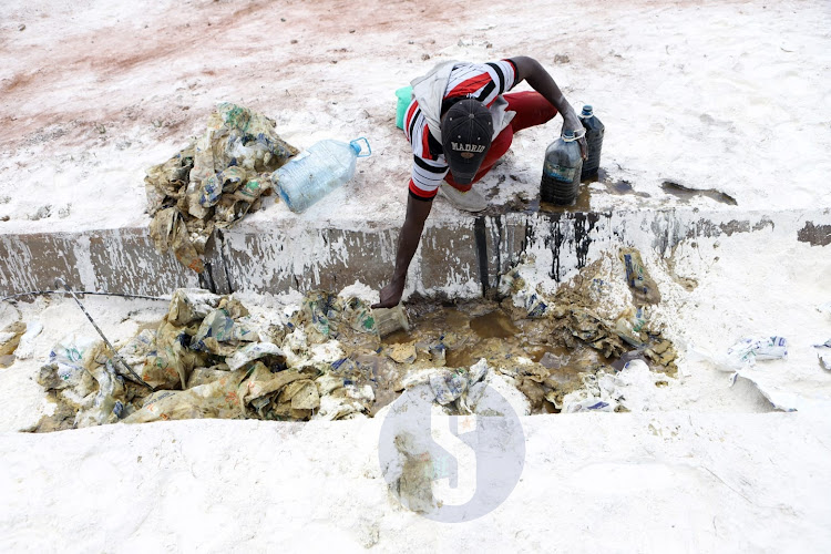 A man scoops oil after a lorry carrying baking flour overturned along Mombasa Road, Nairobi on September 23, 2022.