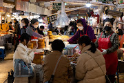 People dine at a food stall in Gwangjang Market in Seoul, South Korea, on Thursday, March 3, 2022. South Korea kicked off two days of early voting on March 4 as the country battles a record wave of coronavirus infections, while data showed inflation unexpectedly accelerated in February as rising costs weighed on voters.  