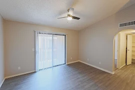 Open living room with vinyl plank flooring, a ceiling fan, sliding patio door with vertical blinds, and tan walls