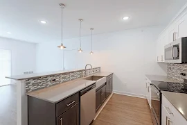 Kitchen with white cabinets, grey countertops, stainless steel appliances, grey tile backsplash, wood floors, three pendants