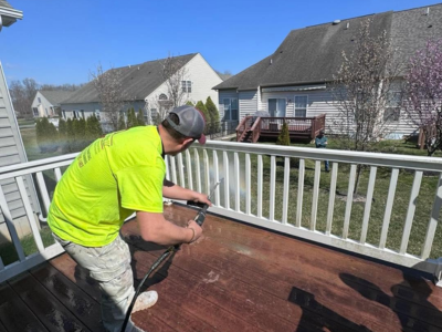 Professional worker in a high-visibility shirt pressure washing white railings on a residential wooden deck.