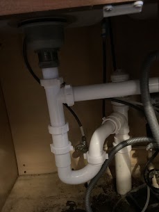 Close-up view of white plastic PVC plumbing pipes and slip-joint connections underneath a kitchen sink.